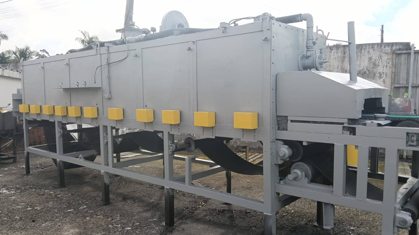 Forno industrial de esteira com estrutura metálica e sistema de exaustão, em pátio de fábrica