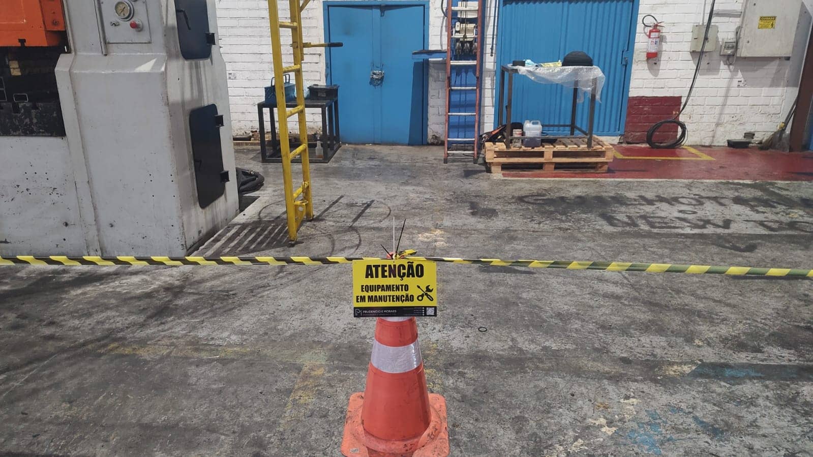 Área de prensa isolada com cone e aviso de equipamento em manutenção